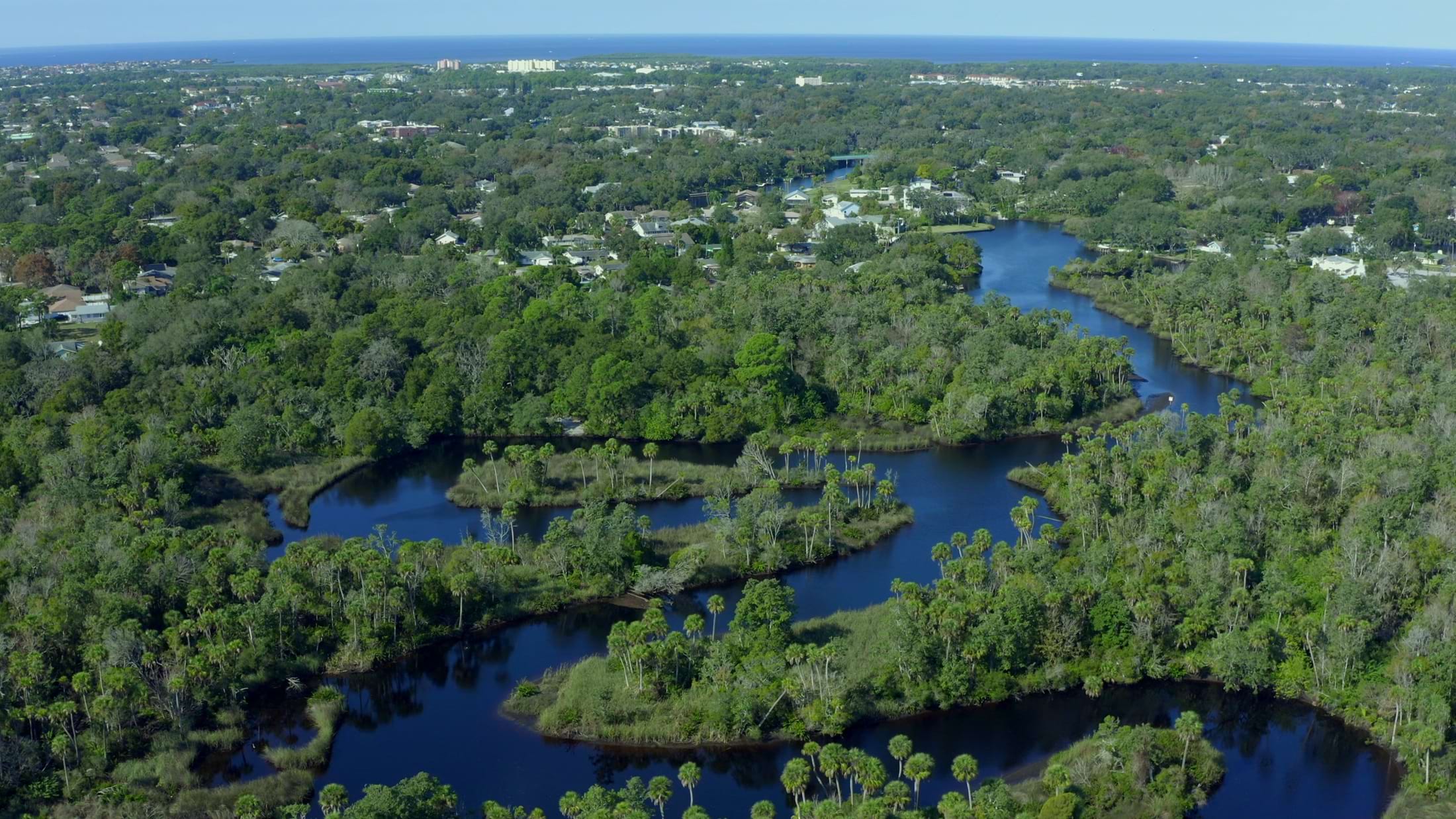 pan-of-river-flowing-through-dense-trees-near-small-town-on-the-gulf-of-mexico-SBI-349418994